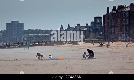 Portobello, Edinburgh, Schottland, Großbritannien. 25. Juni 2020. 2. Tag sehr heißer Witterung, obwohl es kühler war, mit einer kühlen Brise zu beginnen, als es begann, Dampf aufzuheizen, begann aus dem nassen Sand zu steigen und verursachte einen Dunst, die Temperatur erreichte 20 Grad zur Mittagszeit, mehr Leute früher als gestern, Hoffnungsvollusend Sonnenschirm, um sie vor den höheren UV-Strahlen zu schützen, die Wettervorhersagen ungefähr warnen. Stockfoto