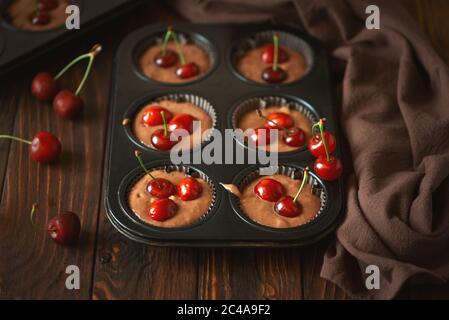 Backen von Schokoladenmuffins. Rohe vegane BananenkirschMuffins mit frischen Beeren auf braunem Holzhintergrund. Draufsicht. Sommeressen Stockfoto