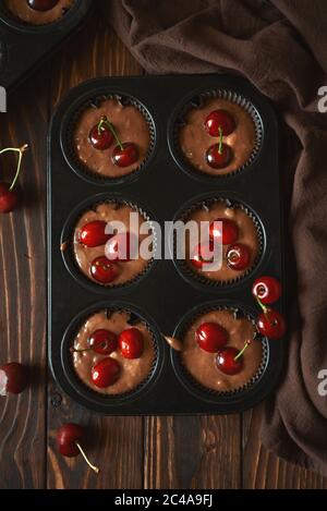 Backen von Schokoladenmuffins. Rohe vegane BananenkirschMuffins mit frischen Beeren auf braunem Holzhintergrund. Draufsicht. Sommeressen Stockfoto