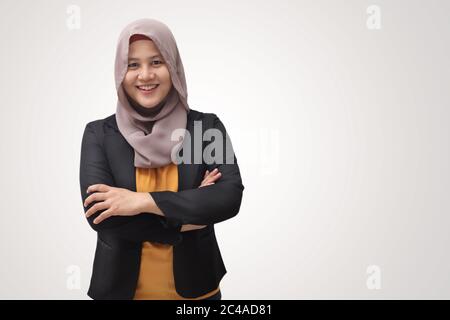 Asiatische muslimische Geschäftsfrau trägt Hijab freundlich lächelnd mit gekreuzten Armen; erfolgreiche selbstbewusste junge Frau; isoliert auf Weiß Stockfoto