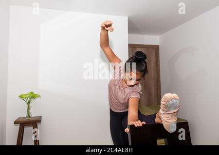 Ein Teenager hebt sein Bein auf einem Stuhl in seinem Wohnzimmer, um Gymnastik, Ballett und Tanzstrecken zu machen Stockfoto