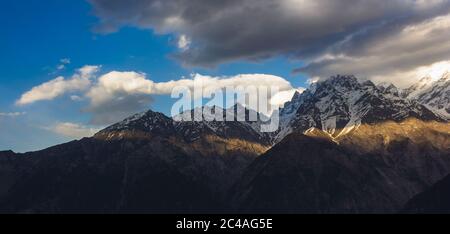 Ein Lichtband trifft die Berge der Kinner Kailash Range mit Wolken, die über dem Dorf Kalpa in Kinnaur, Indien, schweben. Stockfoto