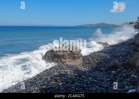 Die Wellen brechen an einem steinigen Strand und bilden einen großen Spray. Großwellen-Crash gegen die Felsen während eines Sturms in den Tropen. Starke Wellen Stockfoto