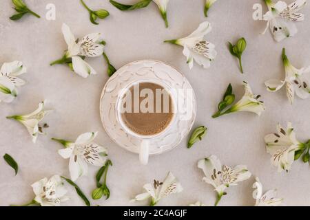 topview Bild des Kaffees in einer weißen rustikalen Tasse über hellgrauem Hintergrund mit weißen Blumen um ihn herum. Stockfoto