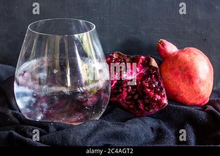 Ein Gin und Tonic, garniert mit einer großen Menge Granatapfelgruben, mit Granatäpfeln, auf schwarzem Hintergrund Stockfoto