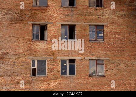 Altes Backsteingebäude aus der Zeit der UdSSR. Sowjetische Architektur. Eine einstürzende Ziegelwand mit kaputten und offenen Fenstern. Ein echtes Wohnviertel Stockfoto