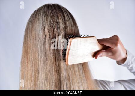 Schöne Frau mit Kamm Bürsten ihre blonden Haare isoliert im Studio weißen Hintergrund. Sorgt für gesundes und sauberes Haar. Konzept des Schönheitssalons Stockfoto