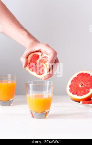 Männliche Hand drückt Grapefruitsaft in einem Glas mit Orangensaft, sommerlich erfrischendes Zitrusgetränk Stockfoto