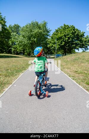 Ein kleiner Junge, der alleine mit Stabilisatoren durch einen Park fährt Stockfoto