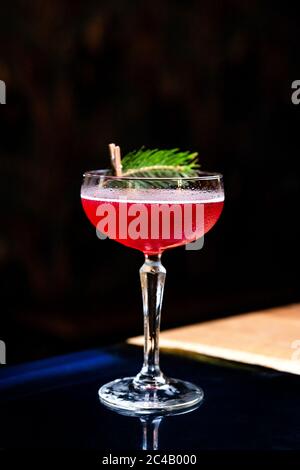 Ein rot-saurer Cocktail in einem Coupé-Glas, dekoriert mit einem Tannenzweig auf dem Tisch in einer Bar Stockfoto