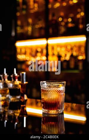 Ein Cocktail in einem altmodischen Glas auf einer Theke mit Spiegelung, Flaschen mit Bittern, Bokeh-Lichter, vertikales Foto Stockfoto