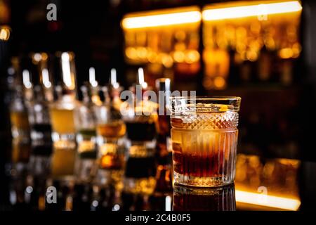 Ein Cocktail in einem altmodischen Glas auf einer Theke mit Spiegelung, Flaschen mit Bittern, Bokeh-Lichter, horizontales Foto Stockfoto