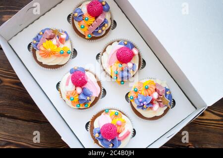 Festliche Schokoladen-Cupcakes mit rosa Frischkäse-Dekoration, goldenen Sternen, Süßigkeiten und Marshmallow in Geschenkbox. Stockfoto