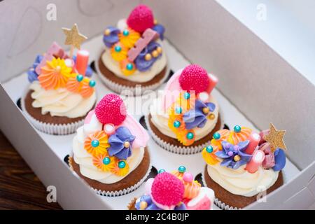 Festliche Schokoladen-Cupcakes mit rosa Frischkäse-Dekoration, goldenen Sternen, Süßigkeiten und Marshmallow in Geschenkbox. Stockfoto