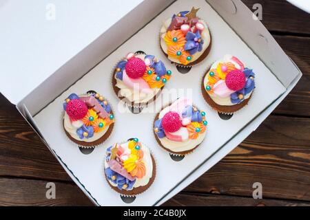 Festliche Schokoladen-Cupcakes mit rosa Frischkäse-Dekoration, goldenen Sternen, Süßigkeiten und Marshmallow in Geschenkbox. Stockfoto