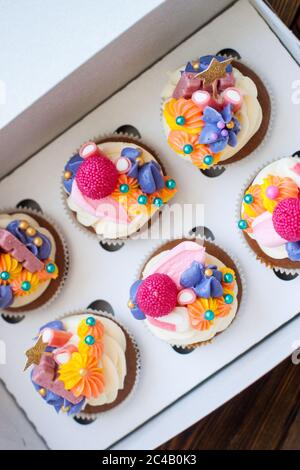 Festliche Schokoladen-Cupcakes mit rosa Frischkäse-Dekoration, goldenen Sternen, Süßigkeiten und Marshmallow in Geschenkbox. Stockfoto