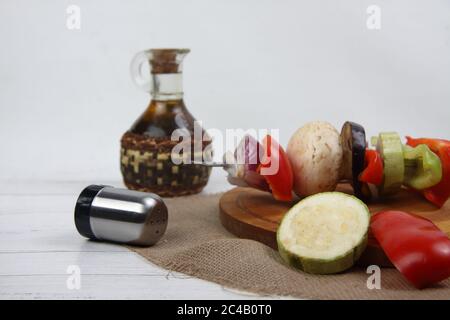 Gemüsestreuer auf dem Schneidebrett, Flasche Salatöl und Salzstreuer auf weißem Holzhintergrund. Das Bild enthält den Kopierbereich Stockfoto