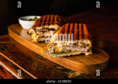 Traditionelles kubanisches Sandwich mit Käse, Schinken und gebratenem Schweinefleisch, serviert auf einem Holzbrett Stockfoto