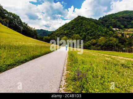 In der Nähe von Cerkno, Küstenregion, Slowenien. Mann, der auf einsamer Straße durch grüne Landschaft geht. Stockfoto