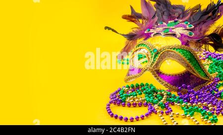 Happy Mardi Gras und Fat Tuesday Karnevalskonzept mit Nahaufnahme auf einer Gesichtsmaske voller Farbe, Federn und Textur und goldenen, grünen und lila Perlen Stockfoto