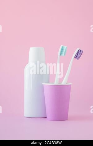 Zwei Zahnbürsten in einem rosa Becher und Mundwasser in einer Flasche auf rosa Hintergrund, Mundhygiene Konzept Stockfoto