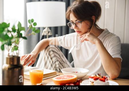 Foto von jungen fokussierten Frau Buch beim Frühstück in gemütlichen Zimmer zu Hause zu lesen Stockfoto