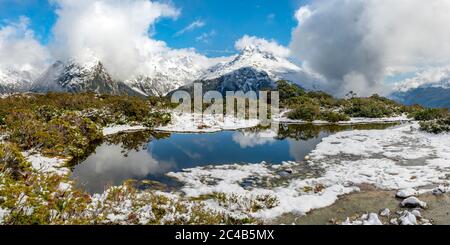 Kleiner Bergsee mit Spiegelung, Blick auf wolkenbedeckte Berge, Schnee auf dem Gipfel des Key Summit, Mt. Christina, Fiordland National Park, West Stockfoto