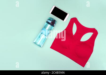 Das Konzept des Home Workouts. Sporttop, Wasserflasche, Telefon auf türkisfarbenem Hintergrund. Flach liegend. Stockfoto