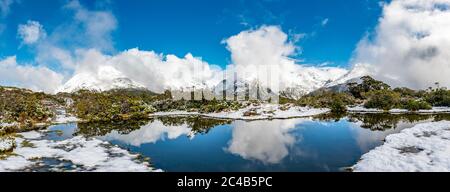 Kleiner Bergsee mit Spiegelung, Blick auf wolkenbedeckte Berge, Schnee auf dem Gipfel des Key Summit, Mt. Christina, Fiordland National Park, West Stockfoto