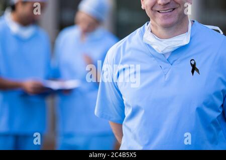 Mittelteil der männlichen Krankenschwester mit schwarzem Band auf Robe lächelnd Stockfoto