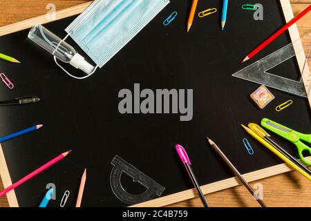 Verschiedene Schulmaterialien, Gesichtsmaske und hydroalkoholisches Gel auf Tafel. Zurück zum Schulkonzept nach der covid19 Pandemie. Stockfoto