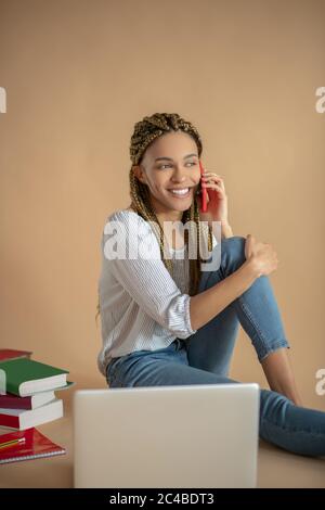 Junge afroamerikanische Frau, die auf dem Boden sitzt, ihr Knie hält und am Telefon spricht Stockfoto