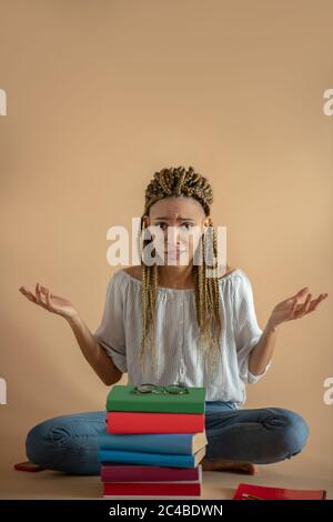 Junge afroamerikanische Frau, die auf dem Boden in Lotuspose vor dem Bücherhaufen sitzt und zuckend abzogt Stockfoto