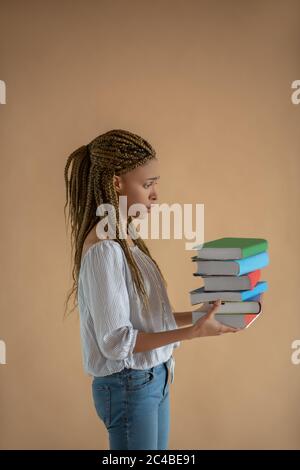 Enttäuschte junge afroamerikanische Frau, die einen Stapel Bücher vor sich trug Stockfoto
