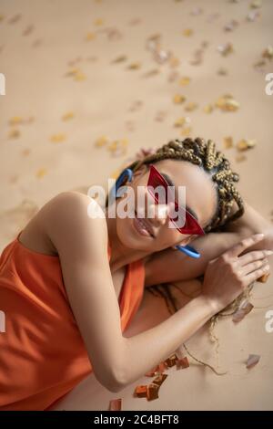 Lächelnde junge Afroamerikanerin, die auf Glitzer liegt und ihren Kopf auf der Hand hält Stockfoto