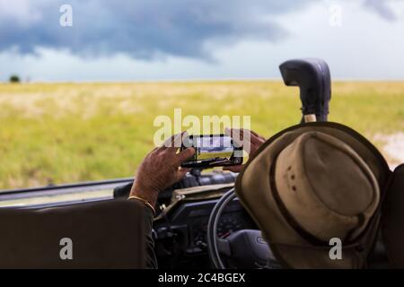 Ein Safari-Guide, der ein Smartphone-Bild von sich nähernden Sturmwolken fotografiert. Stockfoto