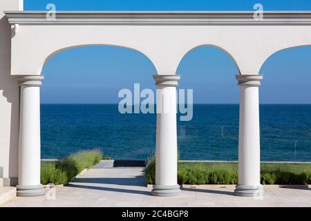 Ein Bogen mit Säulen aus weißem Stein und einem Marmorboden mit Rasen und Blick auf das Meer an der Küste eines luxuriösen Herrenhauses. Stockfoto