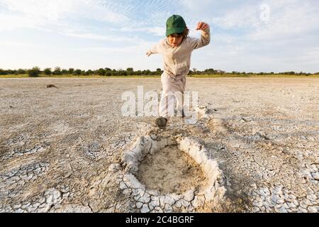 6 Jahre alter Junge, der in Elefantenfußabdrücke springt, Nxai Pan, Botswana Stockfoto