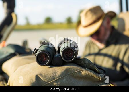 Fernglas auf dem Armaturenbrett eines Safari Jeeps, ein Safari-Führer im Hintergrund. Stockfoto