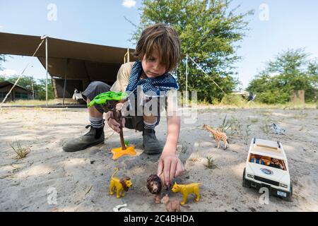 Ein Junge, der eine Safari-Szene mit Spielzeugjeeps und wilden Tierspielzeug und einem hohen Baum aufsetzt Stockfoto