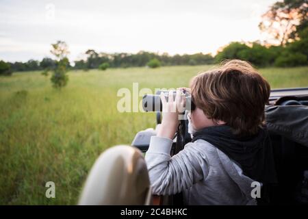 Ein sechsjähriger Junge mit Fernglas in einem Safari-Jeep sitzen. Stockfoto