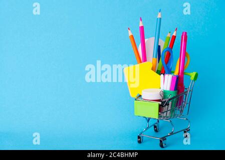 Helle Schreibwaren in einem Mini-Supermarkt-Trolley auf blauem Hintergrund. Zurück zur Schule Konzept Stockfoto