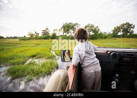 Ein sechsjähriger Junge in einem Safari-Jeep, der durch das Wasser in Sümpfen fährt. Stockfoto