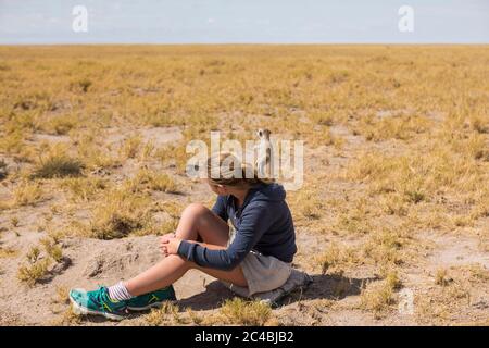 12-jähriges Mädchen, das in der Kalahari-Wüste sitzt und Erdmännchen aus ihren Höhlen auftaucht. Stockfoto