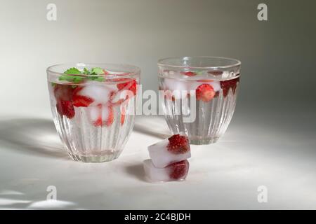Zwei Gläser selbstgemachte Limonade aus gefrorenen Erdbeeren mit Eiswürfeln und Minzblättern auf weißem Hintergrund. Kaltes Getränk. Speicherplatz kopieren. Horiz Stockfoto