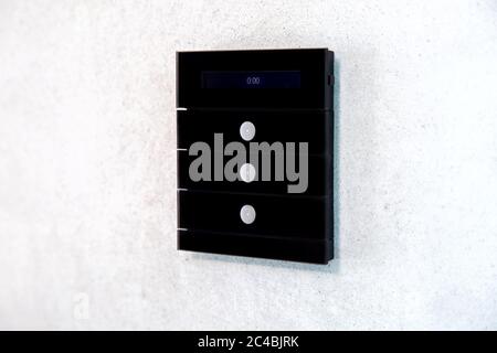 Multifunktions-Lichtschalter zur Steuerung der Funktionen eines Smart Home mit drei Tasten und einem digitalen Display in Schwarz auf einer hellen Wandseite. Stockfoto