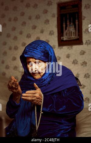 Eine alte muslimische Großmutter betet vor dem Hintergrund des Gebets Mit einem Rosenkranz in den Händen Stockfoto