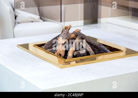 Offener Kamin in der Mitte des Wohnzimmers mit einer Steinplatte und einem Glaskamin Körper, Nahaufnahme des Kamins mit Brennholz und einem Gold fram Stockfoto