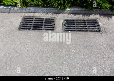 Asphaltstraße mit Sturmabfluss Kanalrost, um Wasser von der Straßenoberfläche Nahaufnahme an einem sonnigen Tag zu beseitigen. Stockfoto