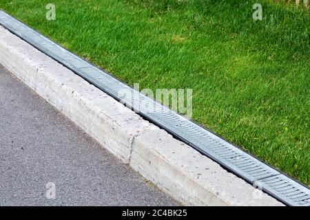 Entwässerungssystem entlang einer Asphaltstraße mit einem Steinpflaster und Grill für Regenwasser in einem grünen Rasen. Stockfoto